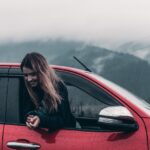 woman is happy and is hanging out of the red car window