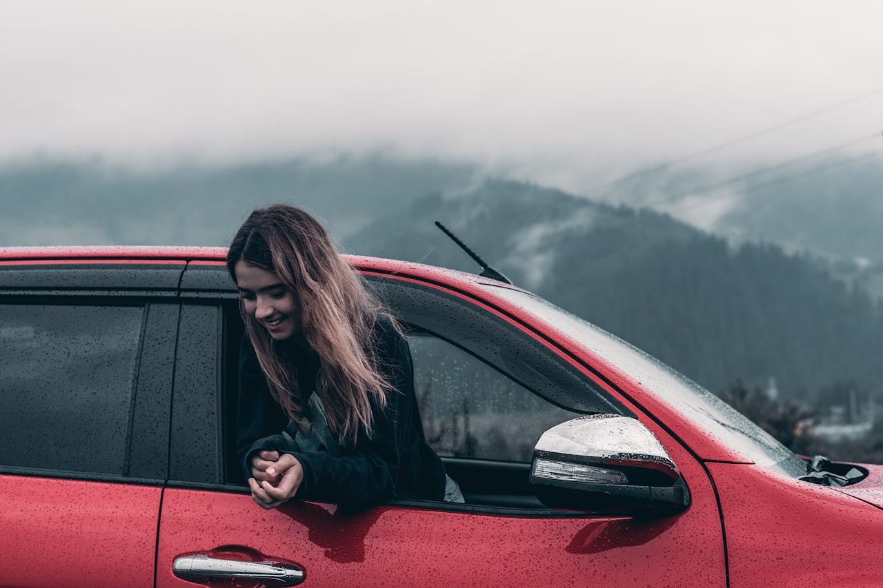 woman is happy and is hanging out of the red car window